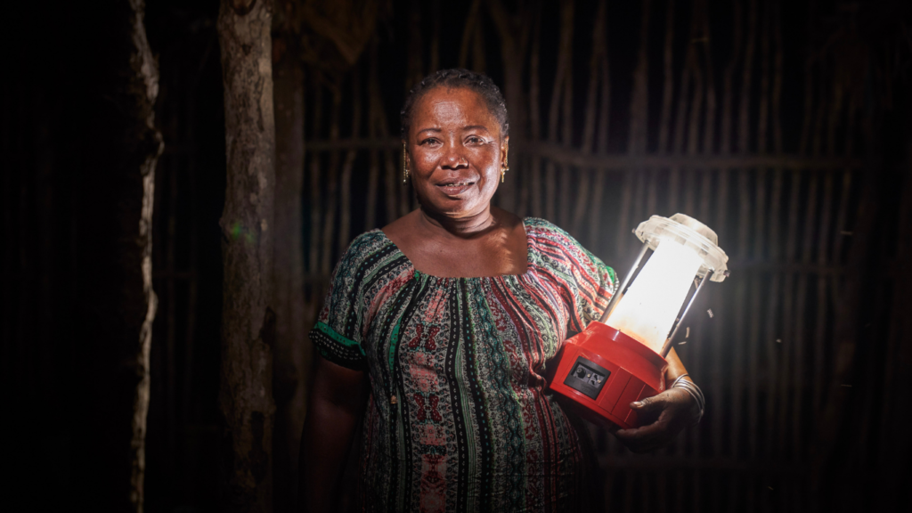 Barefoot College International solar engineer stands holding a lit solar lantern