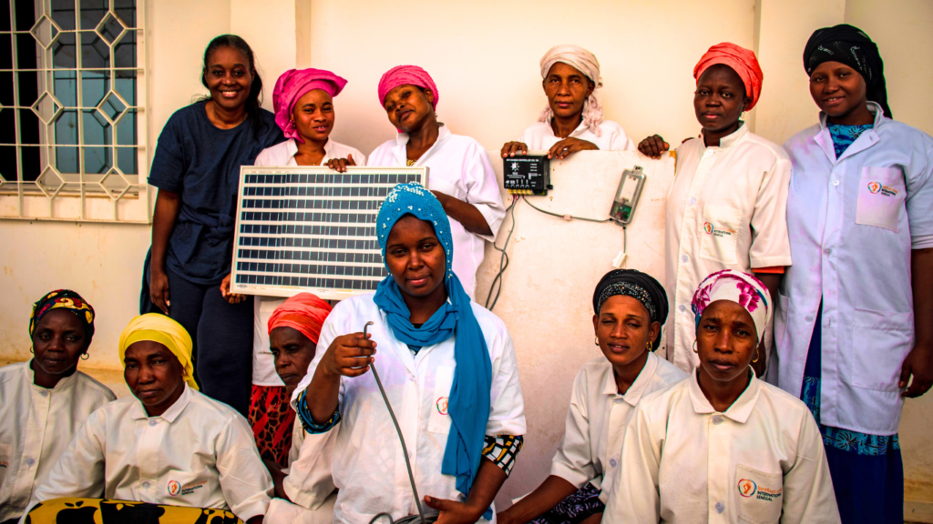 A group of women Solar engineers gather together for a photo, one is holding a solar panel. They are training with Barefoot College International.